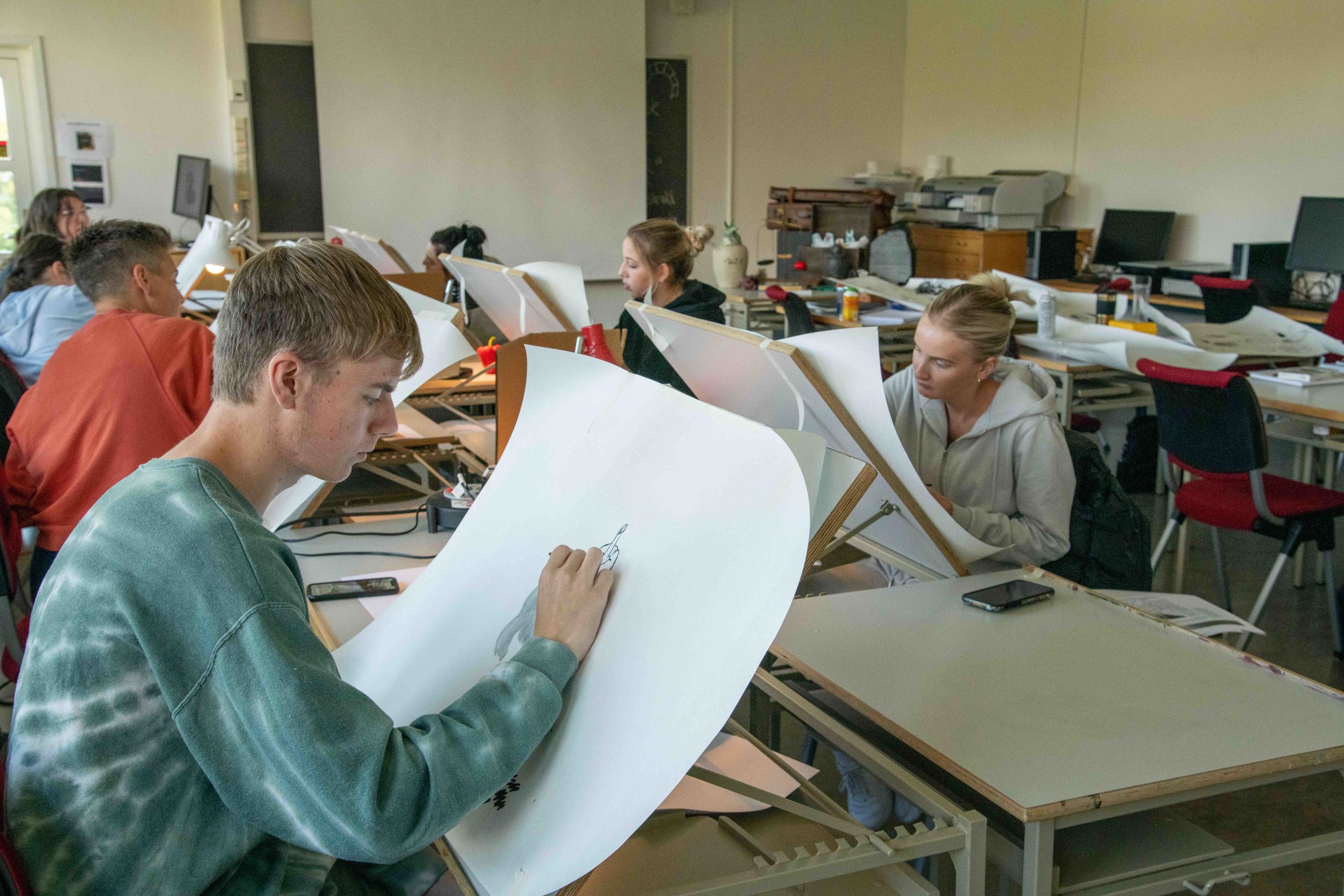 Ein gjeng studentar sit i eit klasserom og teiknar på store ark.