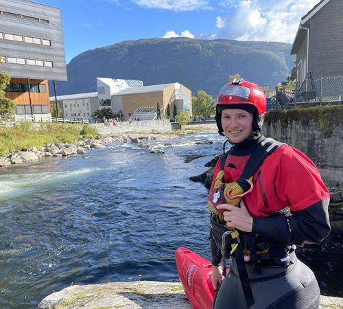 HVL-student Ruben Johnsen Davidsen i padleutstyr, framføre Sogndalselvi og campus Sogndal. 