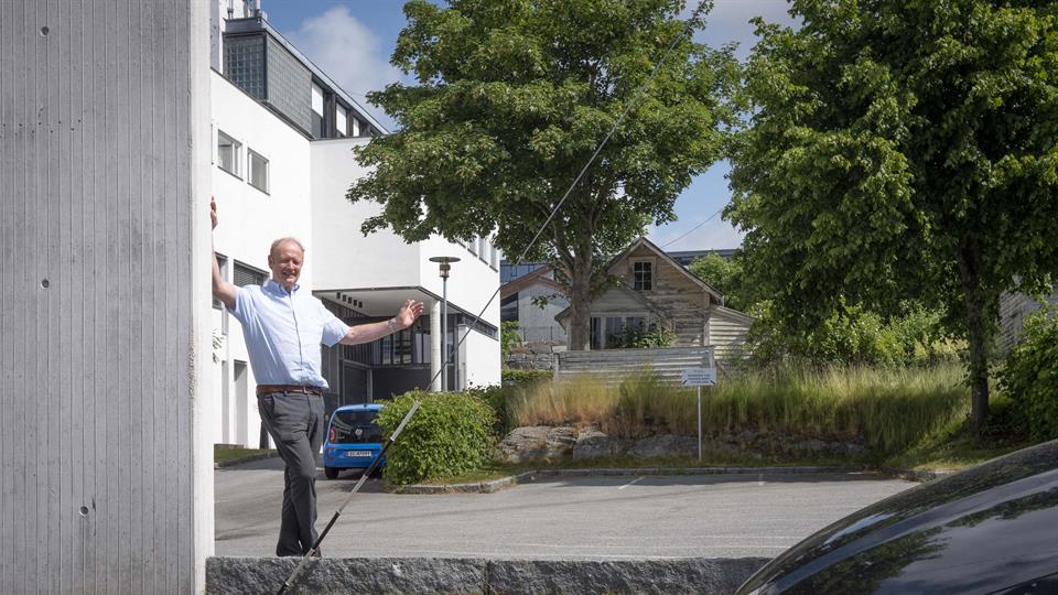 Prosjektleder Knut Kismul står foran en tom, asfaltert parkeringsplass. I bakgrunnen av bildet er det gress, trær og et hvitt trehus.