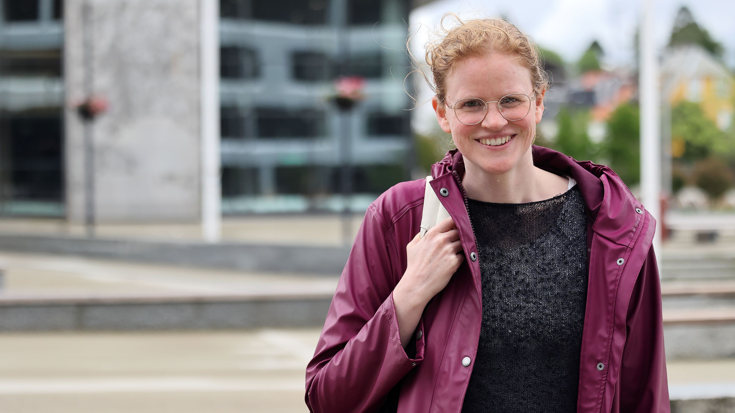 Kvinne står utenfor campus Bergen i regnjakke. Hun smiler. 
