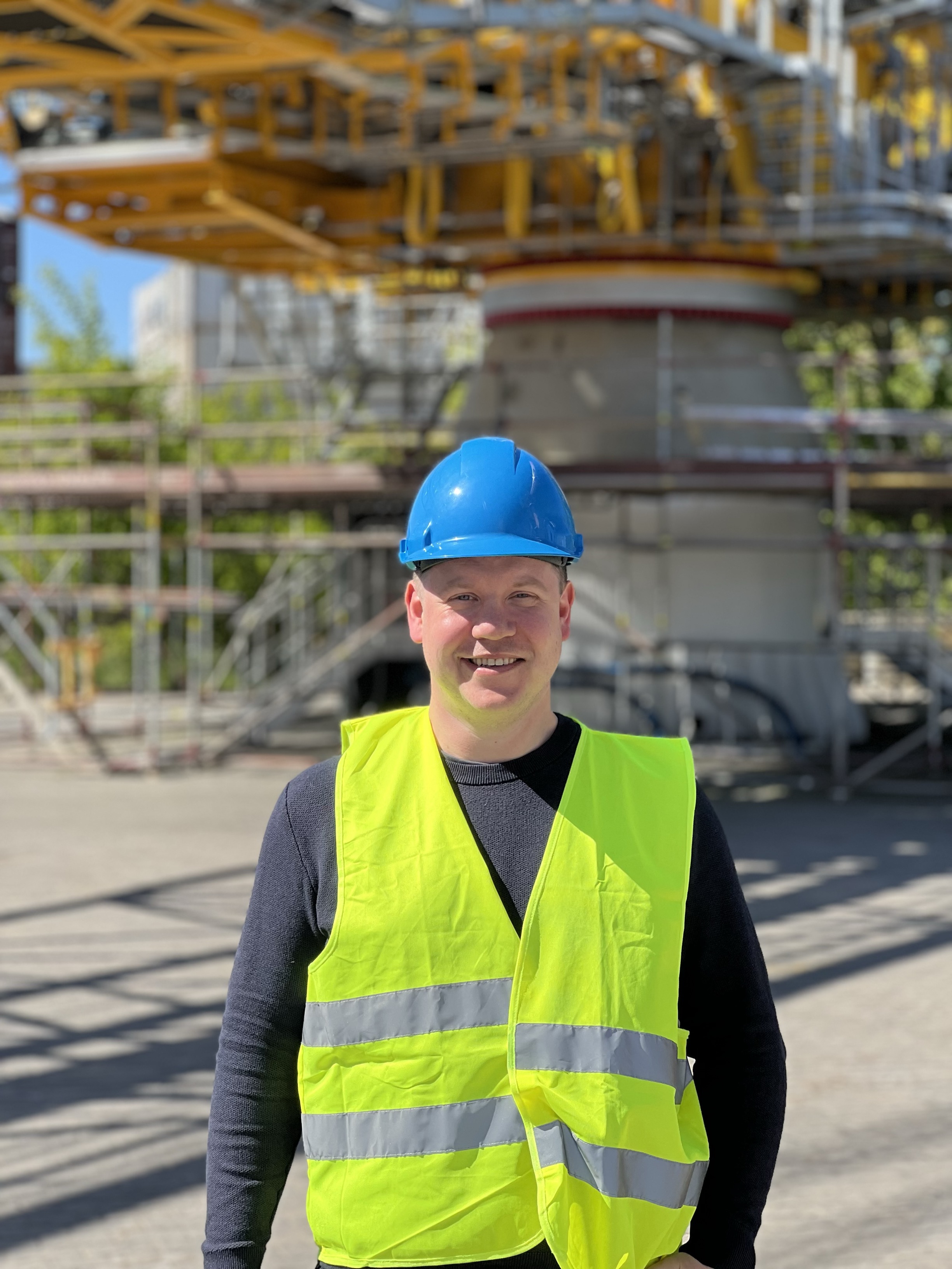 Thorstein Ravneberg Rykkje står smilande framfor ei svær kran. Han har på seg blå arbeidshjelm og gul refleksvest.