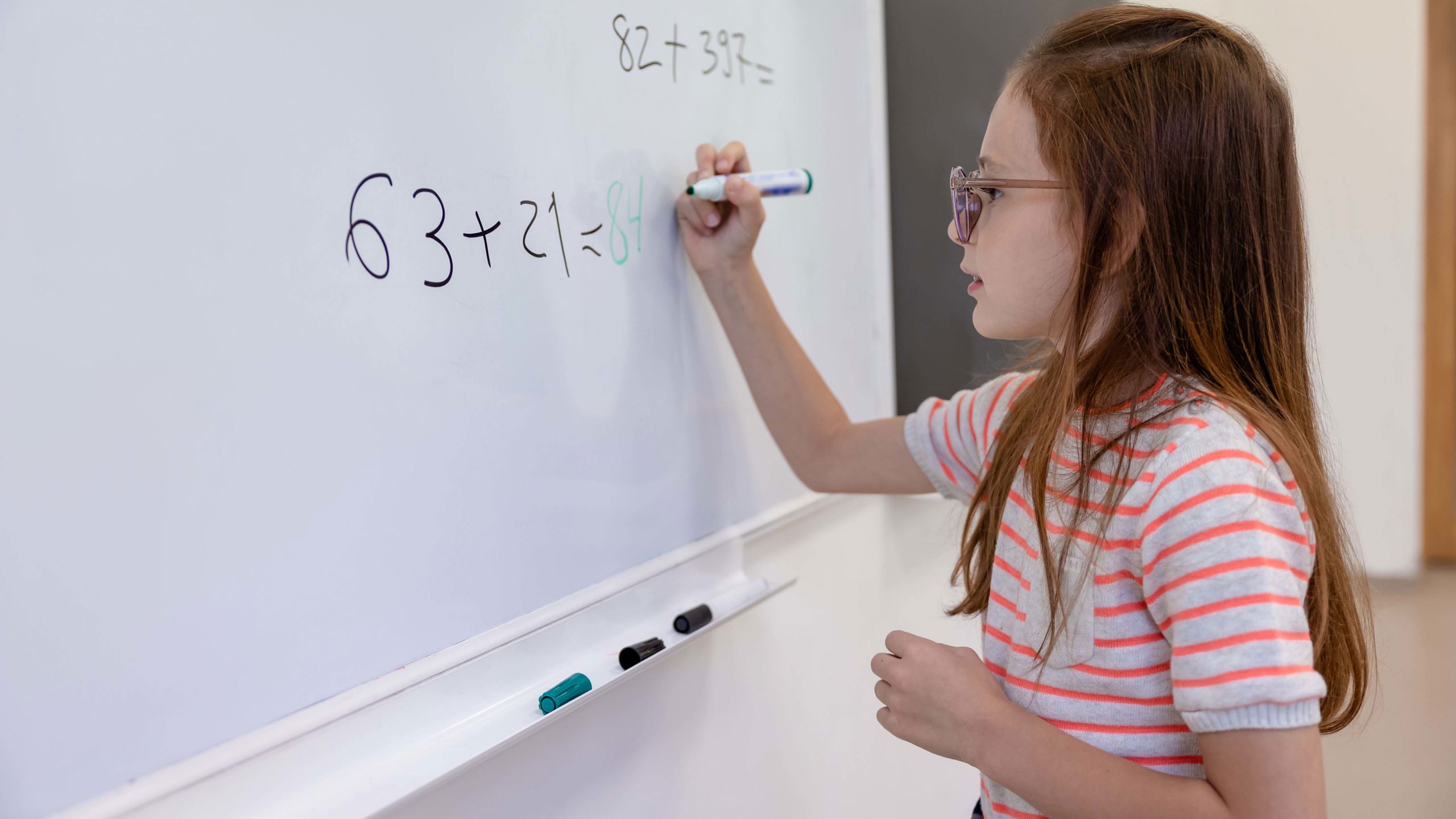 Jente står foran en tavle. På tavlen er det regnestykker i matematikk. 