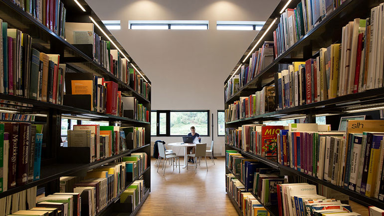 Person sittande i biblioteket blant mange bokhyller. 