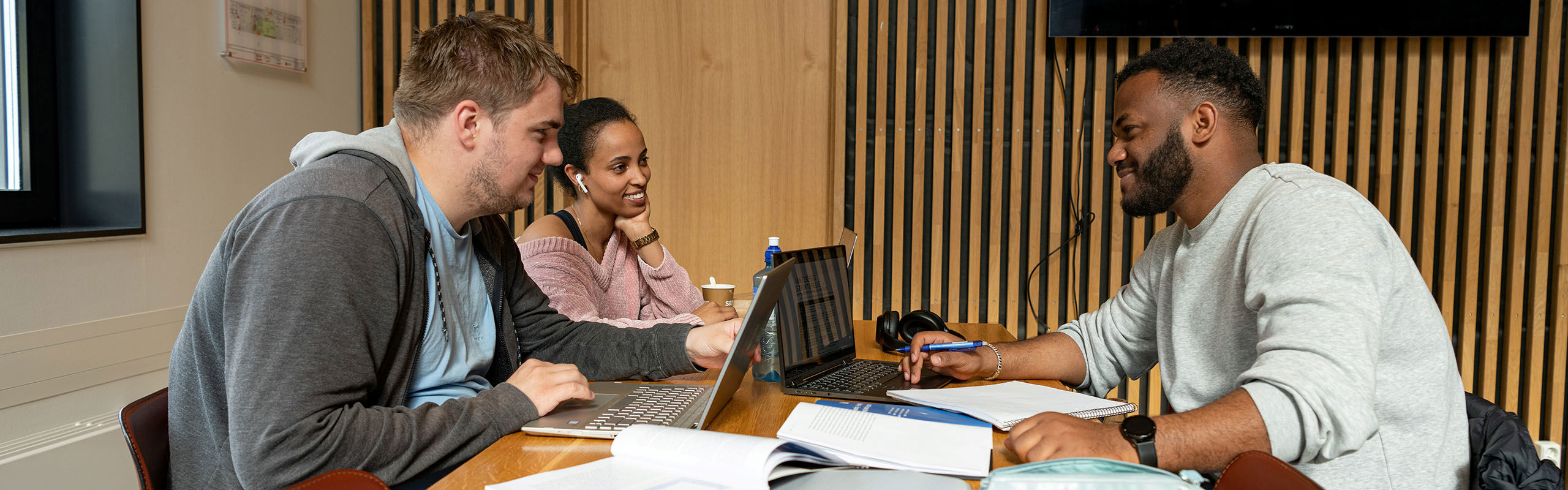 Tre studentar som sit ved bord og jobbar med skulearbeid.
