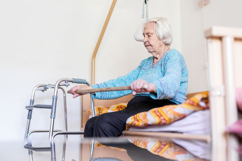 Bildet viser en eldre kvinne som sitter på en seng.