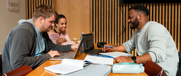 Tre studentar som jobbar ilag med pc og bøker.